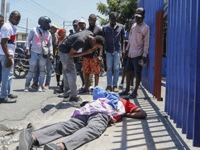 People observe the body of a man lying on the street of the Delmas 30 neighborhood in Port-au-Prince, Haiti, Monday, April 1, 2024. Witnesses reported that he was struck by a stray bullet during a shootout between police and gangs.
