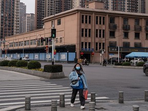 A woman walks past the closed Huanan seafood market on Feb. 9, 2021. Many believe the pandemic began with an animal-to-human transmission at the market, while others espouse the lab-leak hypothesis.