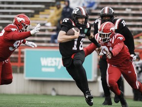 Ottawa Redblacks quarterback Dustin Crum, centre, runs from Calgary Stampeders' Justin Sambu, left, and Cedric Wilcots during second half CFL football action in Calgary