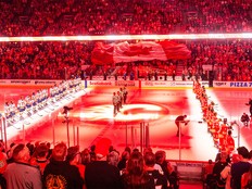 A giant Canadian flag passes over the crowd during O Canada at the Calgary Flames home opener against the St. Louis Blues at the Scotiabank Saddledome on Saturday, Oct. 11, 2025.