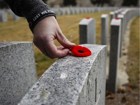 Jamie McIntosh places a poppy on a grave marker at a military cemetery following a Remembrance Day service in Calgary, Friday, Nov. 11, 2016.THE CANADIAN PRESS/Jeff McIntosh ORG XMIT: JMC104