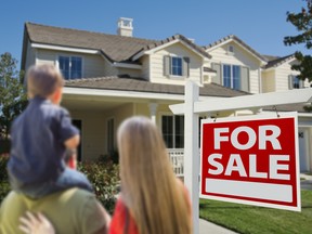 Young Family Looking at a Beautiful New Home with a For Sale Real Estate Sign in Front.