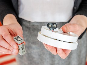 Woman trying to insert a battery in white smoke detector - the device that senses smoke, typically as an indicator of fire