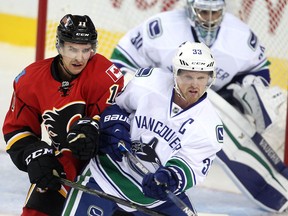 Mikael Backlund of the Calgary Flames jousts with Vancouver Canucks captain Henrik Sedin in front of goalie Ryan Miller in the first period of the season opener Wednesday October 7, 2015 at the Saddledome.