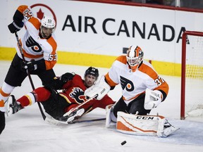 Philadelphia Flyers goalie Brian Elliott follows a loose puck as the Calgary Flames' Troy Brouwer, centre, is knocked to the ice by Shayne Gostisbehere during second-period NHL hockey action in Calgary on Monday. Photo by Jeff McIntosh/THE CANADIAN PRESS.