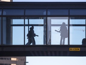 Pedestrians pass a busker as they cross Fifth Avenue S.W. on the plus-15 in Calgary, on January 12, 2016.