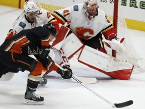 Anaheim Ducks left wing Andrew Cogliano, front, backhands a shot against Calgary Flames defenseman Travis Hamonic, left, and goaltender Mike Smith, right, during the third period of an NHL hockey game in Anaheim, Calif., Friday, Dec. 29, 2017. The Ducks won 2-1.