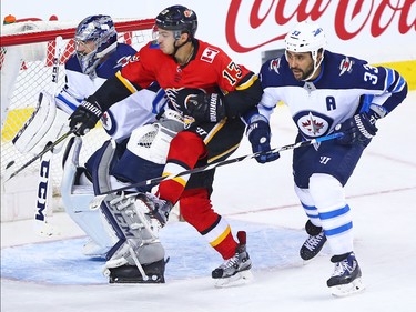 The Calgary Flames Johnny Gaudreau fights past Dustin Byfuglien and goaltender Connor Hellebuyck during NHL action at the Scotiabank Saddleome in Calgary on Saturday January 20, 2018.