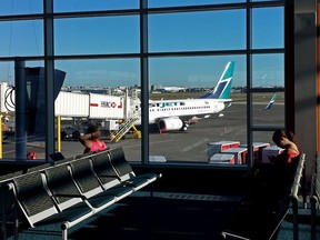 Passengers wait for a flight in the Vancouver International Airport terminal with a WestJet 737-700 seen out the window on Sept. 20, 2014.