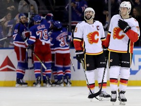 Mark Giordano (No.  5) and Mark Jankowski (No. 77) of the Calgary Flames react after the go-ahead goal by Mika Zibanejad (No. 93) of the New York Rangers in the third period during their game at Madison Square Garden on February 9, 2018 in New York City.