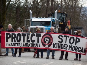 Protesters hold a banner as a transport truck attempting to deliver heavy equipment to Kinder Morgan sits idle as others block a gate at the company's property in Burnaby, B.C., on Monday, March 19, 2018. Two federal politicians say they will join demonstrations in Burnaby, B.C., opposing construction of the federally approved Kinder Morgan pipeline expansion.