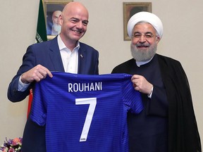 A handout picture released by the office of Iranian President Hassan Rouhani shows him and FIFA President Gianni Infantino holding a football shirt with Rouhani's name on March 1, 2018. (Getty Images)