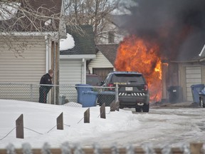 A Calgary police officer takes cover as a garage where a gunman was holed up in catches fire. Photo by Zach Laing, Postmedia Network