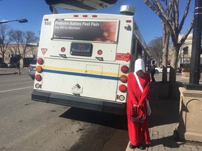 A woman dressed in a costume from The Handmaid's Tale stands behind a bus featuring an anti-abortion ad in Lethbridge, Alta.