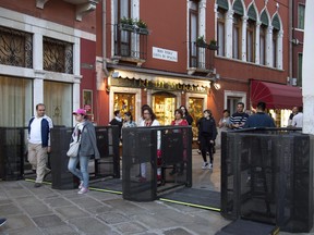 In this photo taken on Friday, April 27, 2018, people walk through gates in Venice, Italy. Venice has resorted to installing gates at the ends of two bridges to turn back tourists if their numbers become overwhelming. The temporary measure was put in place Saturday in the lagoon city for a four-day holiday weekend culminating on Labor Day, May 1. (Riccardo Gregolin/ANSA via AP)