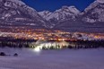 The Town of Canmore is lit up at night with fog rising from the Bow River below.