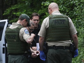 Washington State Fish and Wildlife Police confer with an individual from the King County Medical Examiner's and a King County Sheriff's deputy on a remote gravel road above Snoqualmie, WA., following a fatal cougar attack. Saturday May 19, 2018. (Alan Berner /The Seattle Times via AP)