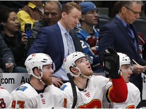Calgary Flames coach Glen Gulutzan, back, watches as the Flames face the Colorado Avalanche during the first period of an NHL hockey game Wednesday, Feb. 28, 2018, in Denver.