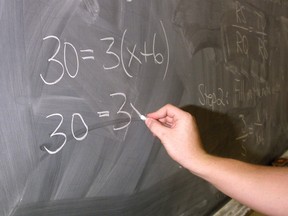 A teacher writes math problems on a chalkboard.