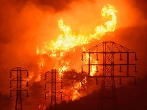 In this Dec. 16, 2017, file photo provided by the Santa Barbara County Fire Department, flames burn near power lines in Sycamore Canyon near West Mountain Drive in Montecito, Calif.