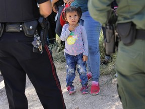 A Mission Police Dept. officer (L), and a U.S. Border Patrol agent watch over a group of Central American asylum seekers before taking them into custody on June 12, 2018 near McAllen, Texas.