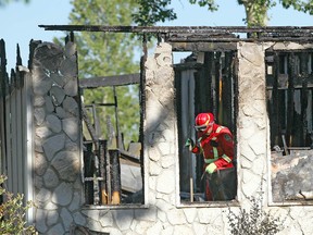 A Fire investigator searches through a burned out house on Lake Ere Estate in Chestermere, east of Calgary after an early morning fire Tuesday, June 12, 2018. Chestermere RCMP confirm that they are investigating the death of an adult male who was located on the property. The death is preliminary, it is not considered suspicious. Jim Wells/Postmedia