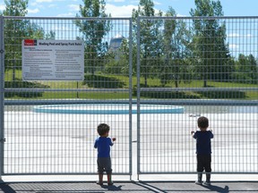David and Na'im Yagi peer through a locked fence outside the wading pool and spray park in northeast Calgary on Tuesday, June 12, 2018. The two boys were with their dad Emmanuel and the family is disappointed the pool wont be open. The wading pool at Prairie Winds Park won't hold water due to a leak and the City is unsure wher it is. Jim Wells/Postmedia