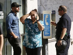 An unidentified Trader Joe's supermarket employee, center, talks on her phone as Los Angeles Police evacuate a group of witnesses after a gunman barricaded himself inside the store in Los Angeles Saturday, July 21, 2018. Police believe a man involved in a standoff at the Los Angeles supermarket shot his grandmother and girlfriend and then fired at officers during a pursuit before he crashed into a utility pole outside the supermarket and ran inside the store. About three hours after he took hostages in the store, the suspect surrendered.