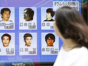 A woman walks on a street while watching TV news reporting executions of six members of Aum Shinrikyo, in Tokyo Thursday, July 26, 2018.
