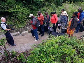 A Royal Canadian Mounted Police officer, left, standing in Saint-Bernard-de-Lacolle, Quebec, advises migrants that they are about to illegally cross from Champlain, N.Y., and will be arrested, Monday, Aug. 7, 2017.