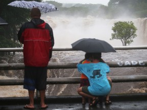 People gather on a bridge to watch the Wailuku River flood waters on Hawaii's Big Island on Aug. 23, 2018 in Hilo. Hurricane Lane has brought more than a foot of rain to some parts of the island.