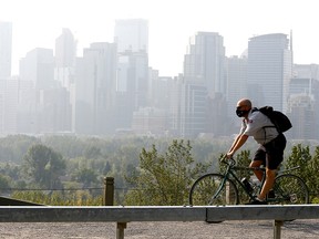 Jerry Hoult from Canada Post rides by the smokey cityscape on Crescent Hill as smoke has thickened in Calgary on Wednesday August 8, 2018. Darren Makowichuk/Postmedia