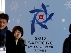 FILE - In this Thursday, Feb. 16, 2017 file photo, people walk by a poster for the Sapporo Asian Winter Games, displayed at the main media center in Sapporo on Japan's northern island of Hokkaido. The Japanese city of Sapporo has dropped its bid to host the 2026 Winter Olympics following a recent earthquake. The International Olympic Committee says the city will now focus on a bid for the 2030 Games.