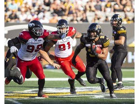 Hamilton Tiger-Cats running back Sean Thomas-Erlington carries the ball as Calgary Stampeders defensive linemen Michael Kashak and Mike Rose give chase during first-half CFL action in Hamilton on Saturday.