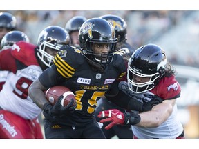 Hamilton Tiger-Cats running back Alex Green (15) tries to fend off defender Calgary Stampeders line backer Alex Singleton (49) during second half CFL Football game action in Hamilton, Ontario on Saturday, September 15, 2018.