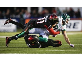 Saskatchewan Roughriders' Patrick Lavoie, right, is brought down by Calgary Stampeders' Tre Roberson, top, and Jamar Wall during CFL football action in Calgary, Saturday, Oct. 20, 2018.