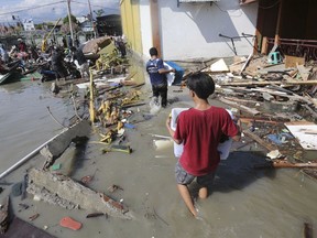 People carry items from a shopping mall badly damaged by a massive earthquake and tsunami in Palu, Central Sulawesi, Indonesia, Sunday, Sept. 30, 2018.