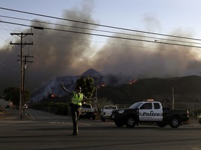 A police officer mans a checkpoint in front of an advancing wildfire Thursday, Nov. 8, 2018, near Newbury Park, Calif. The Ventura County Fire Department has also ordered evacuation of some communities in the path of the fire, which erupted a few miles from the site of Wednesday night's deadly mass shooting at a Thousand Oaks bar.