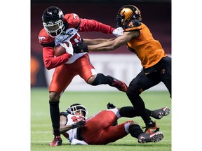 Calgary Stampeders' Bakari Grant, left, steps over Eric Mezzalira, bottom, as he tries to fight off B.C. Lions' Garry Peters, right, during the first half of a CFL football game in Vancouver, on Saturday November 3, 2018.