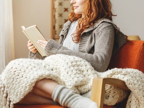 Happy young woman wrapped in a blanket reading a book in a chair