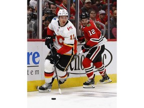CHICAGO, ILLINOIS - DECEMBER 02: Mikael Backlund #11 of the Calgary Flames looks to pass in front of Alex DeBrincat #12 of the Chicago Blackhawks at the United Center on December 02, 2018 in Chicago, Illinois. The Flames defeated the Blackhawks 3-2.
