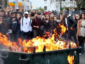 Students watch a burning trash bin outside their school in Bayonne, southwestern France, Thursday, Dec.6, 2018. Protesting students are disrupting schools and universities Thursday, and drivers are still blocking roads around France, now demanding broader tax cuts and government aid.