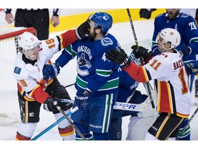 Calgary Flames' Matthew Tkachuk, left, gets his glove in the face of Vancouver Canucks' Erik Gudbranson, centre, as Calgary's Mikael Backlund, of Sweden, watches during second period NHL hockey action in Vancouver on Saturday, Feb. 9, 2019.