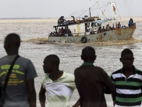 A group of men watch the arrival of a boat carrying displaced families rescued from a flooded area of Buzi district, 200 kilometers (120 miles) outside Beira, Mozambique, on Saturday, March 23, 2019. A second week has begun with efforts to find and help some tens of thousands of people in devastated parts of southern Africa, with some hundreds dead and an unknown number of people still missing.
