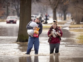 Anthony Thomson, left, and Melody Walton make their way out of a flooded neighbourhood Sunday, March 17, 2019, in Fremont, Neb.