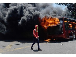 An opposition demonstrator walks near a bus in flames during clashes with soldiers loyal to Venezuelan President Nicolas Maduro after troops joined opposition leader Juan Guaido in his campaign to oust Maduro's government, in the surroundings of La Carlota military base in Caracas on April 30, 2019.