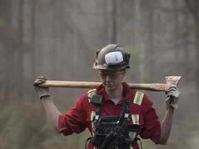 A firefighter carries an axe to battle northwest Alberta wildfires near the town of High Level on Friday, May 24, 2019. About 5,000 people in High Level and surrounding communities have been out of their homes since the long weekend, as the Chuckegg Creek fire rages three kilometres outside the town.