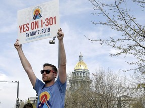 Chris Olson holds a sign near a busy intersection in downtown Denver on Monday, May 6, 2019, as he urges voters to decriminalize the use of psilocybin, the psychedelic substance in "magic mushrooms."