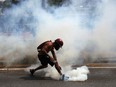 An anti-government protester grabs a tear gas canister launched by National Guard forces outside La Carlota airbase during clashes between the two sides in Caracas, Venezuela, Wednesday, May 1, 2019. Opposition leader Juan Guaido called for Venezuelans to fill streets around the country Wednesday to demand President Nicolas Maduro's ouster. Maduro is also calling for his supporters to rally.