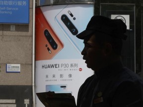 In this photo taken Thursday, May 16, 2019, a man handing out pamphlets is silhouetted against a advertisement for the latest smartphones from Huawei in Beijing.